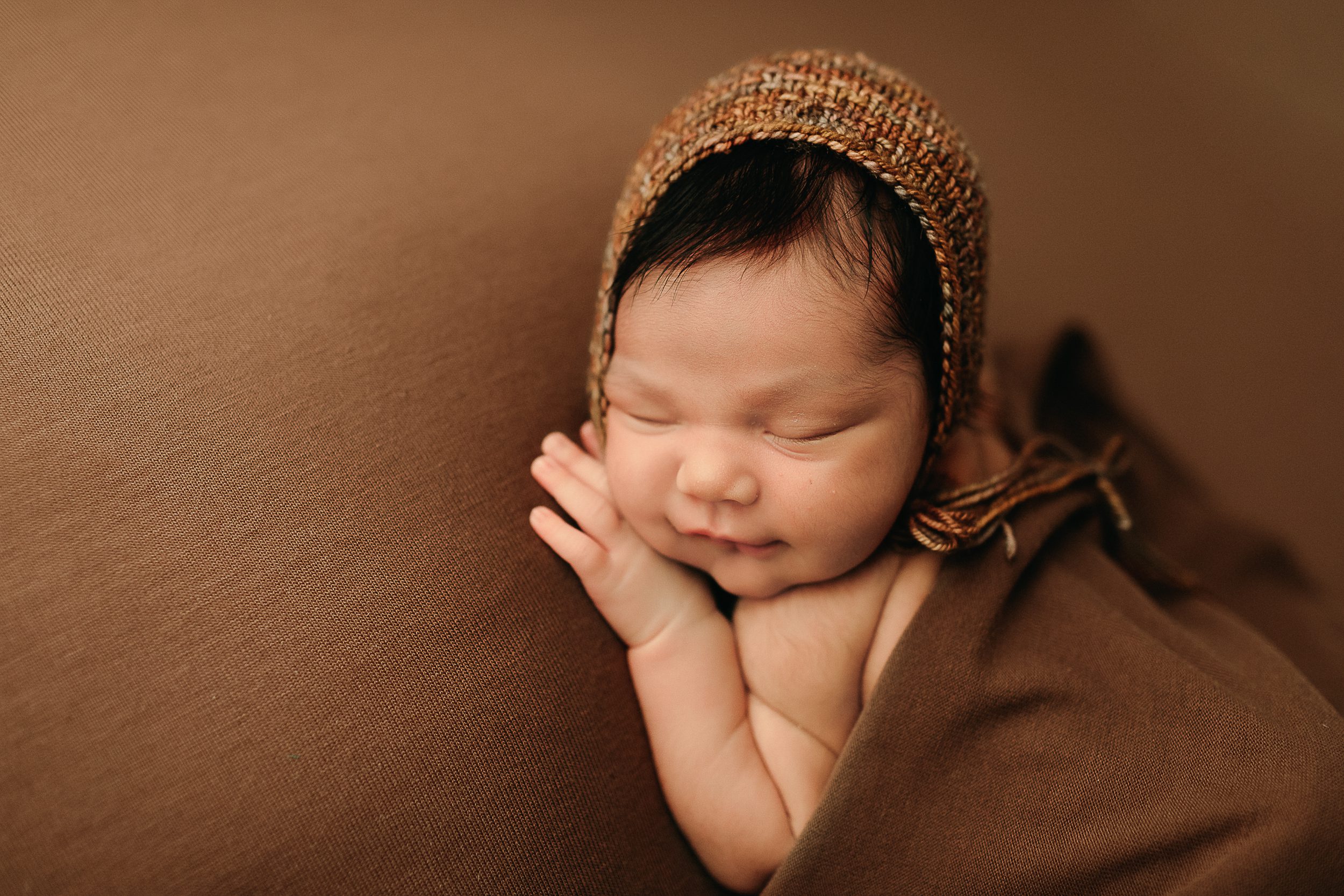newborn baby born wearling a bonnet on a brown backdrop.