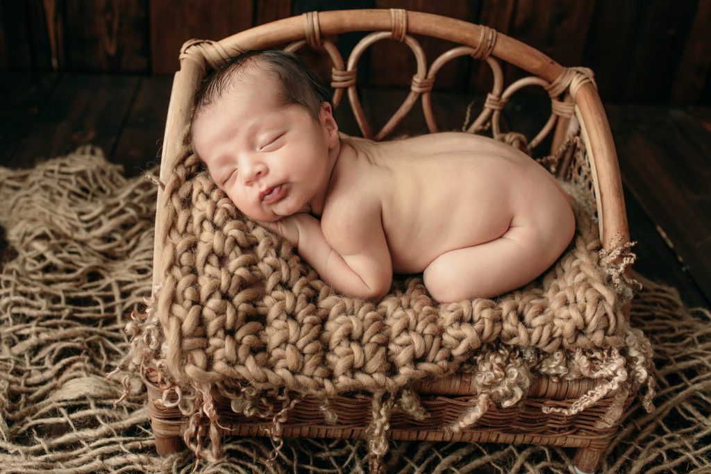 Newborn baby boy lying on his stomach on top of a brown rattan baby bed.