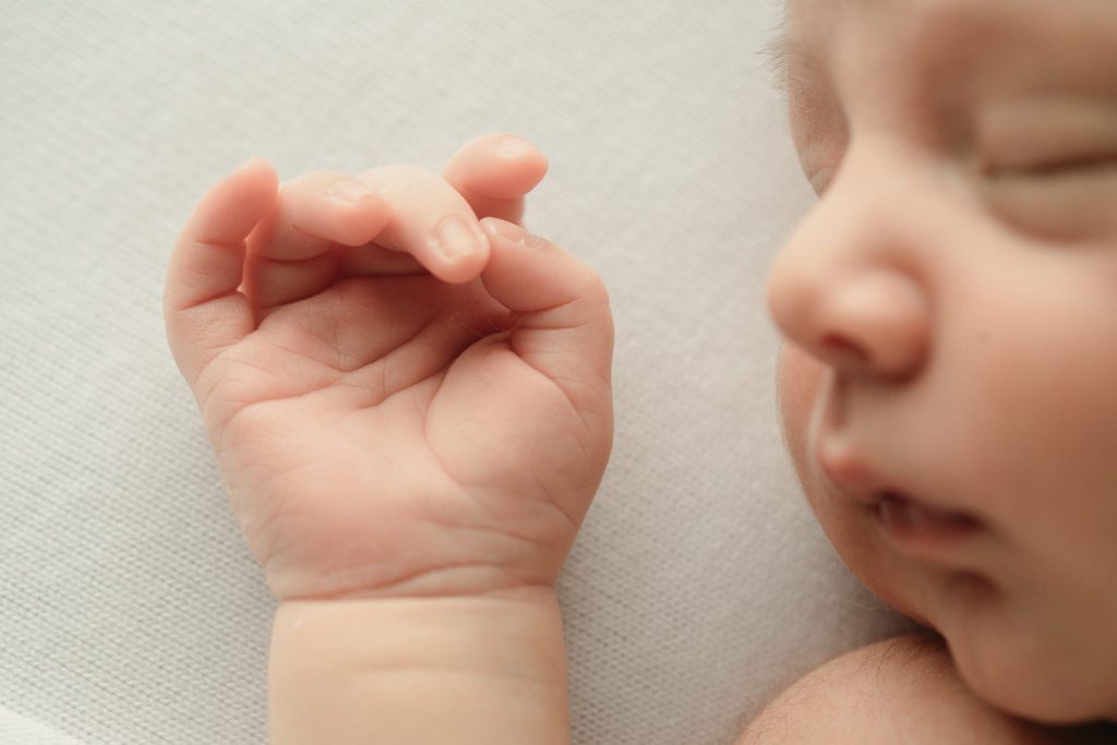 Detail image of a newborn baby boy hand in focus and his face in the background blurred.
