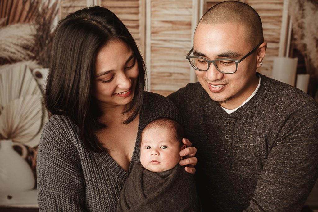 Mom and dad wearing posing with their newborn baby boy his photo shoot.